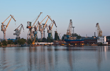 Obraz premium Shipyard with colorful cranes in early morning near loading docks.