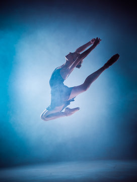 The silhouette of young ballet dancer jumping on a blue backgrou