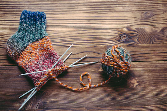 Knitted sock, ball of yarn and knitting needles on a wooden surf
