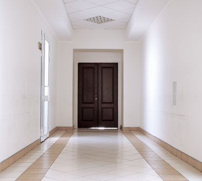 White hallway with marble floor and brown door in hospital background