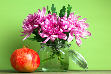 juicy pomegranate with flowers in a vase of water on wooden table on green background