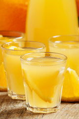 Orange juice with fruit pieces in small cups and a jug on old wo