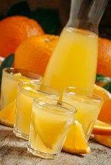 Orange juice with fruit pieces in small cups and a jug on old wo