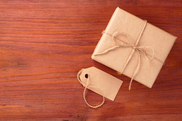 Gift box into brown paper tied by twine and blank tag on old wooden table with space for text