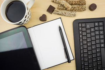 Opened blank notebook with tablet, pen, keyboard  and cup of coffee, on wooden desktop.