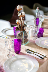 Decorated table ready for dinner. Beautifully decorated table set with flowers, candles, plates and serviettes for wedding or another event in the restaurant.