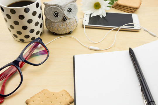 Opened blank notebook with pen, smartphone and cup of coffee and cookies, on wooden desktop.