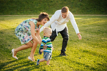 Happy family playing on the lawn in the Summer - parents catching their little son.