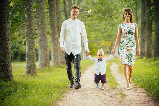Mother and father holding hands with their little son walking on the forest road. 