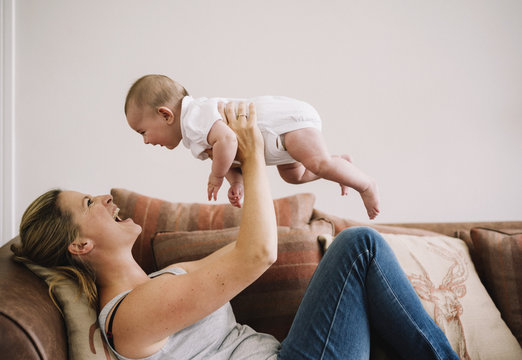 A woman lying on a sofa playing with a baby girl. 