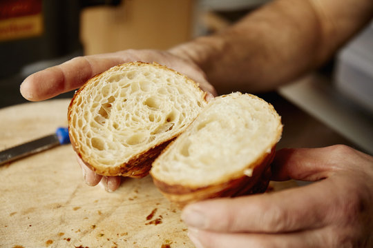 A man holding a croissant cut in half, to show the light layered texture of the cooked dough. 
