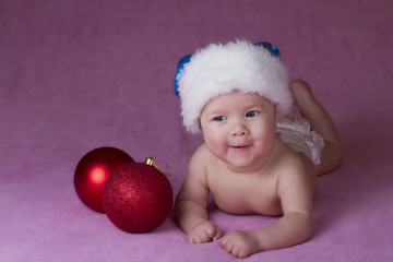 Joyful little baby in Christmas hat and Christmas decoration on a pink background 