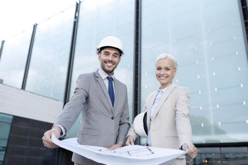 smiling businessmen with blueprint and helmets