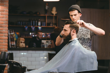 Young barber making haircut of  bearded man in barbershop