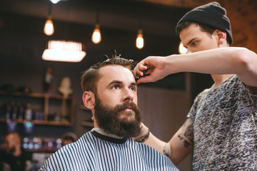 Skillful barber cutting hair of young man with beard