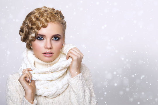 portrait of a beautiful young blonde woman on a light background. hair tied in a braid. girl wearing a warm sweater and scarf. copy space..
