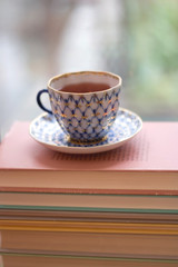 Tea in a vintage porcelain cup on a pile of old books. Selective focus.