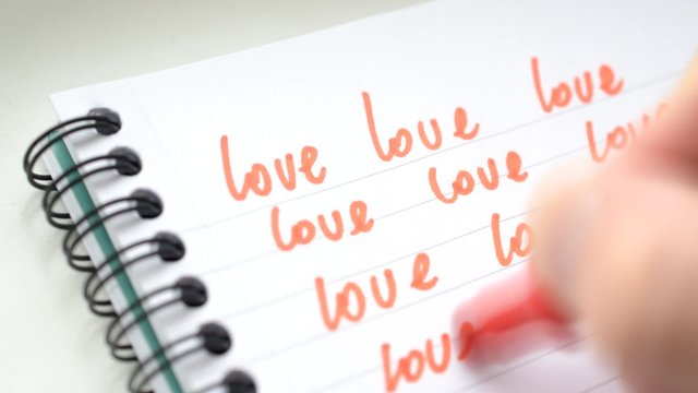 Time lapse of writing word LOVE many times with red marker or felt tip pen on lined white paper in a writing pad. High key macro shot with shallow depth of field