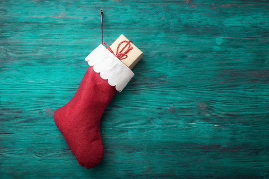 Red Santa sock with gift box over wooden background