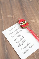 Christmas greeting in several languages written on white paper on wooden background