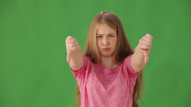 Frowning young woman standing on green background shaking her head no and showing thumbs down