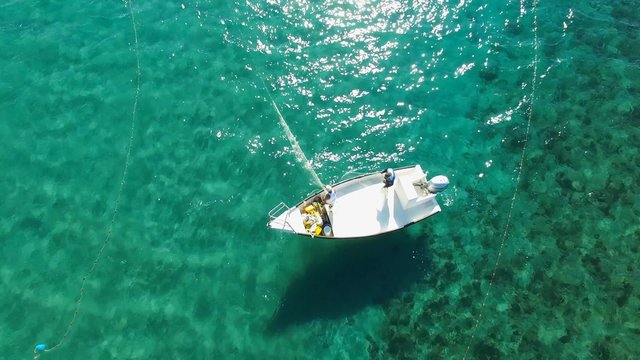 Aerial footage of men on a small fishing boat deploying a fishing net into the water