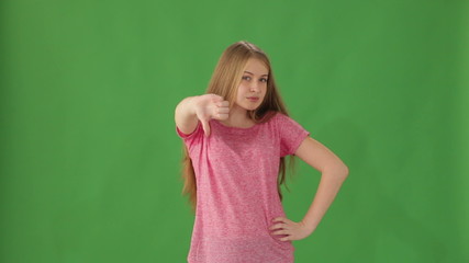 Young woman standing on green background showing thumb down and shaking her head no