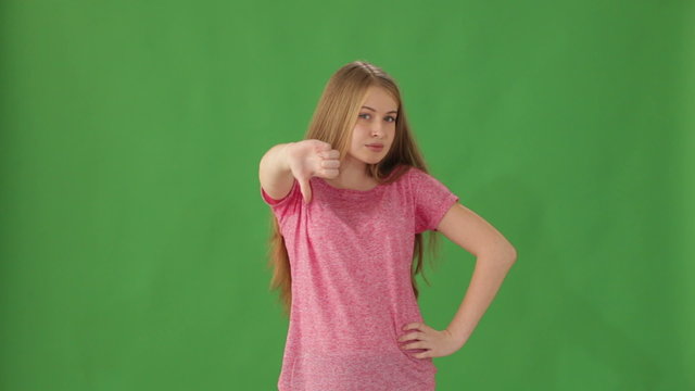 Young woman standing on green background showing thumb down and shaking her head no