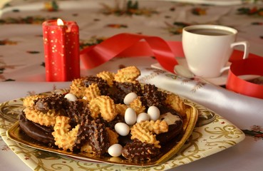 Detail of delicious Christmas cookies with cup of coffee on a table with candle in red tone