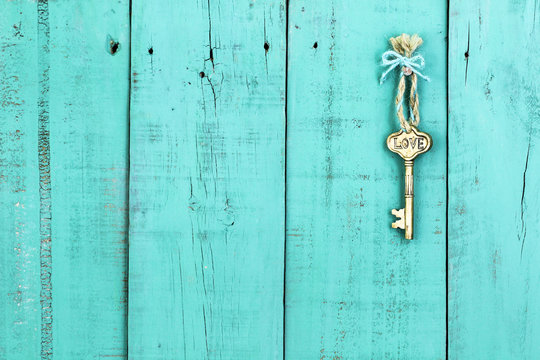 Brass skeleton key with Love hanging by rope on antique rustic teal blue wood door