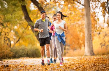 A lively group of young friends enjoys a refreshing jog in the park during the vibrant autumn season, relishing the camaraderie and the crisp, cool air.
