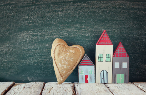 image of vintage wooden colorful house and fabric heart on wooden table in front of blackboard
