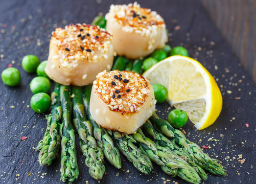 Fried scallops with sesame seeds, asparagus, lemon and green peas on a black plate