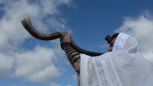 Jewish man blow Shofar (horn) outdoors under the sky, on the Jewish High Holidays in Rosh Hashanah and Yom Kippur