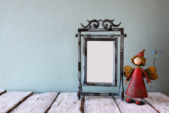low key image of old victorian steel blue blank frame and cute fairy on wooden table
