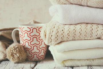 Fototapeta na wymiar Stack of white cozy knitted sweaters next to cup of coffee on a wooden table. faded retro style image