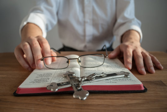Clergyman in white shirt sitting at the table with prayer book, glasses and crucifix. Cold morning light.