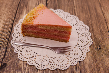 Fresh tasty sweet piece of pink cake on a white napkin and a dessert fork on a wooden background