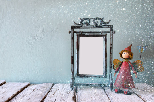low key image of old victorian steel blue blank frame and cute fairy on wooden table. glitter overlay
