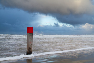 Beach pole with red head at high tide under a dark cloud