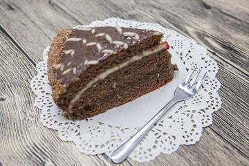 Fototapeta na wymiar Fresh tasty sweet piece of chocolate cake on a white napkin and a dessert fork on a wooden background