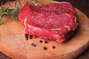 Fresh raw beef steak on wooden background decorated with rosemary and pepper