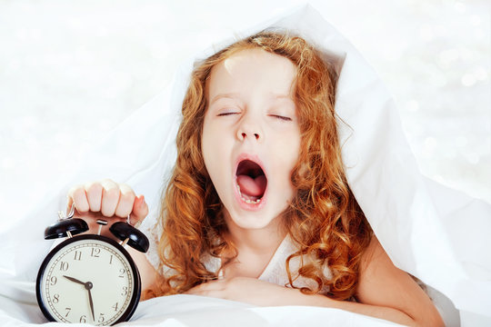Curly girl yawn and holding alarm clock.