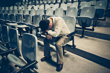 Businessman sitting desperately in the middle of the stair path with rows of chairs along both sides