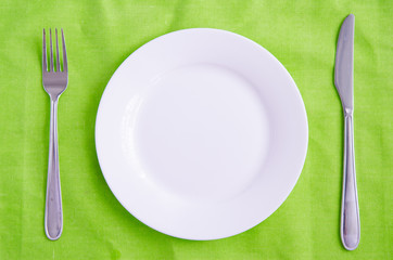 Empty plate, fork and knife on green background