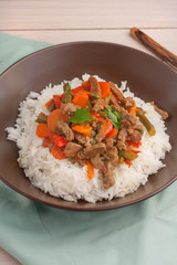 a brown bowl of white rice with stir fry beef with bell peppers, asparagus and carrots