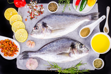 Fresh raw gilthead fishes with lemon, herbs, salt on black background. Healthy food concept. Food frame