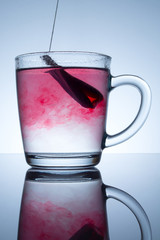 tea bag in a transparent mug with beautiful abstract stains in water with reflection on a grey background
