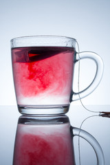 tea bag in a transparent mug with beautiful abstract stains in water with reflection on a grey background
