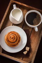 cinnamon roll,  cup of coffee and cream  on wooden tray